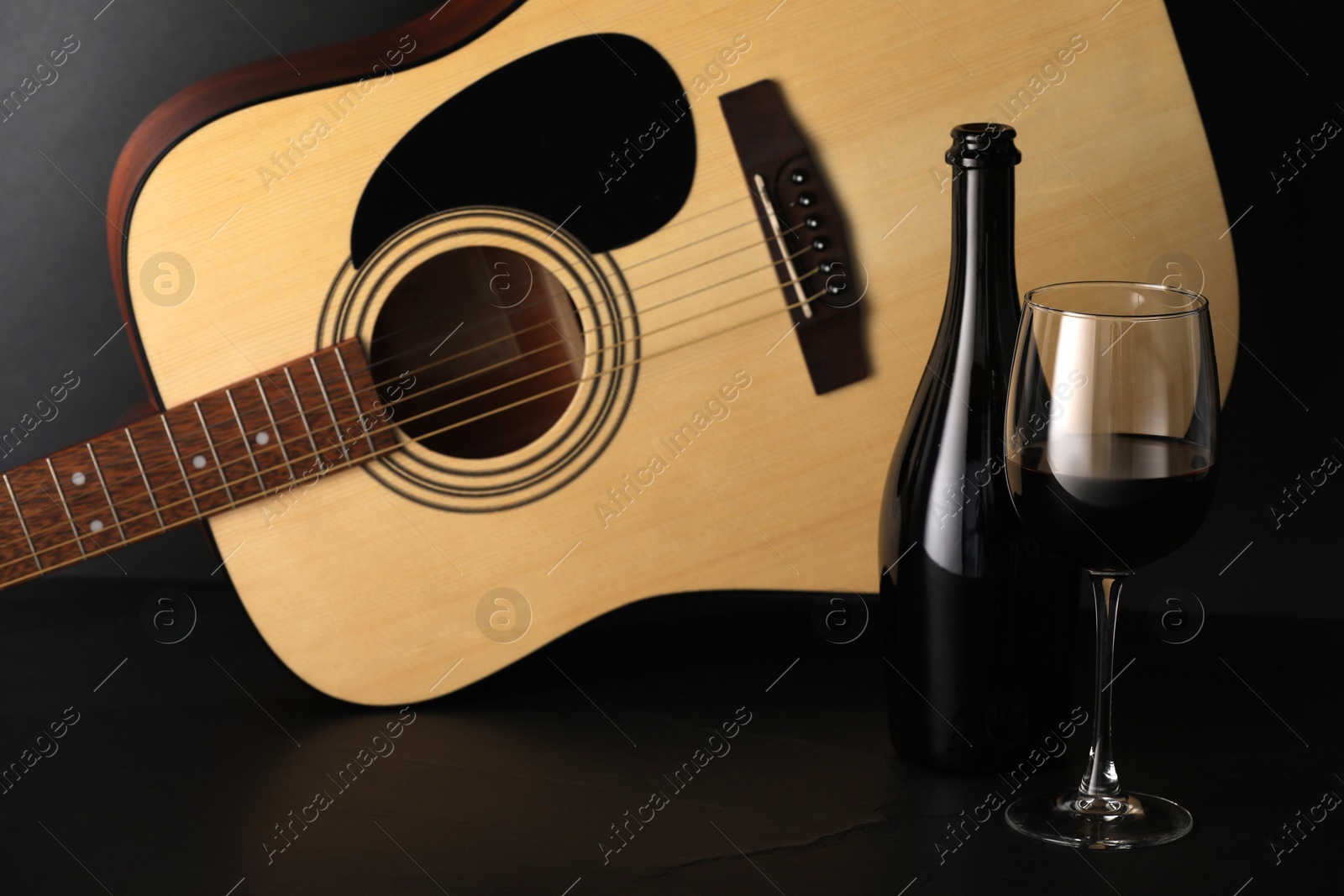 Photo of Acoustic guitar and red wine on black table, closeup