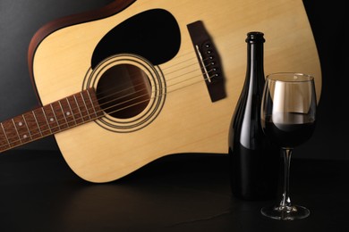 Photo of Acoustic guitar and red wine on black table, closeup