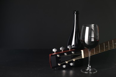 Photo of Acoustic guitar and red wine on black table, closeup. Space for text