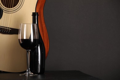 Photo of Acoustic guitar and red wine on black table, closeup. Space for text