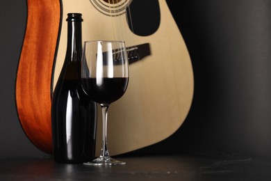 Photo of Acoustic guitar and red wine on black table, closeup