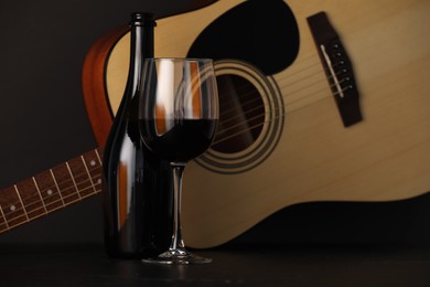Photo of Acoustic guitar and red wine on black table, closeup