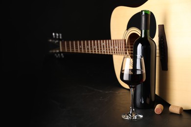 Photo of Acoustic guitar and red wine on black table, closeup