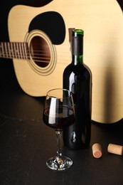 Photo of Acoustic guitar and red wine on black table, closeup