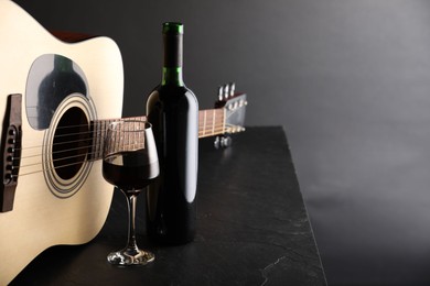 Photo of Acoustic guitar and red wine on black table, closeup. Space for text