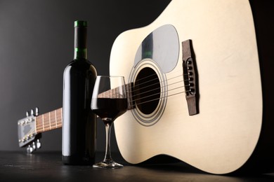 Photo of Acoustic guitar and red wine on black table, closeup