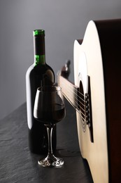 Photo of Acoustic guitar and red wine on black table, closeup
