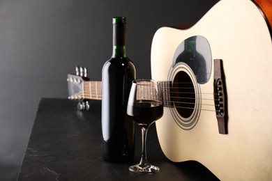Photo of Acoustic guitar and red wine on black table, closeup
