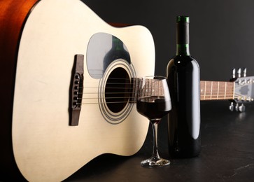 Photo of Acoustic guitar and red wine on black table, closeup