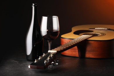 Photo of Acoustic guitar and red wine on black table with brown light, closeup