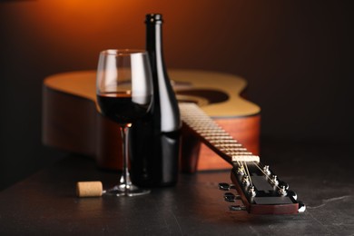 Photo of Acoustic guitar and red wine on black table with brown light, closeup