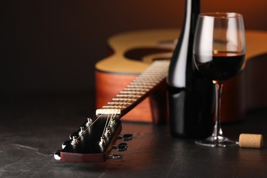 Photo of Acoustic guitar and red wine on black table with brown light, closeup