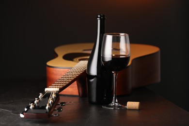 Photo of Acoustic guitar and red wine on black table, closeup