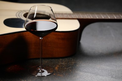 Photo of Acoustic guitar and red wine on black table, closeup