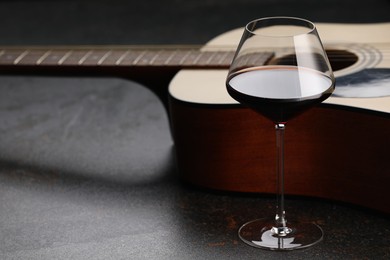 Photo of Acoustic guitar and red wine on black table, closeup