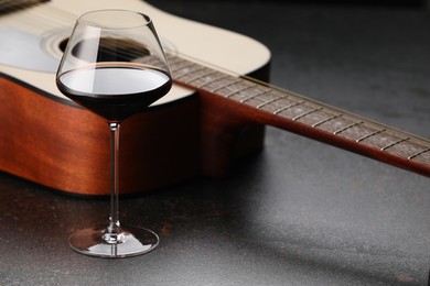 Photo of Acoustic guitar and red wine on black table, closeup