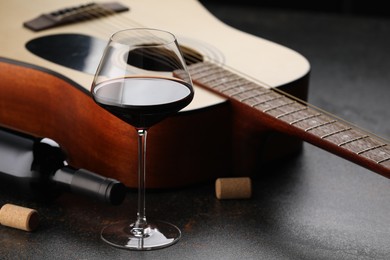 Photo of Acoustic guitar and red wine on black table, closeup