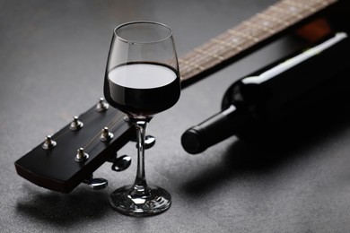 Photo of Acoustic guitar and red wine on black table, closeup
