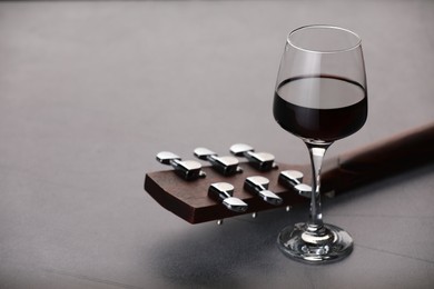 Photo of Acoustic guitar and red wine on grey table, closeup. Space for text