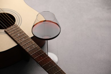 Photo of Acoustic guitar and red wine on grey table, closeup. Space for text