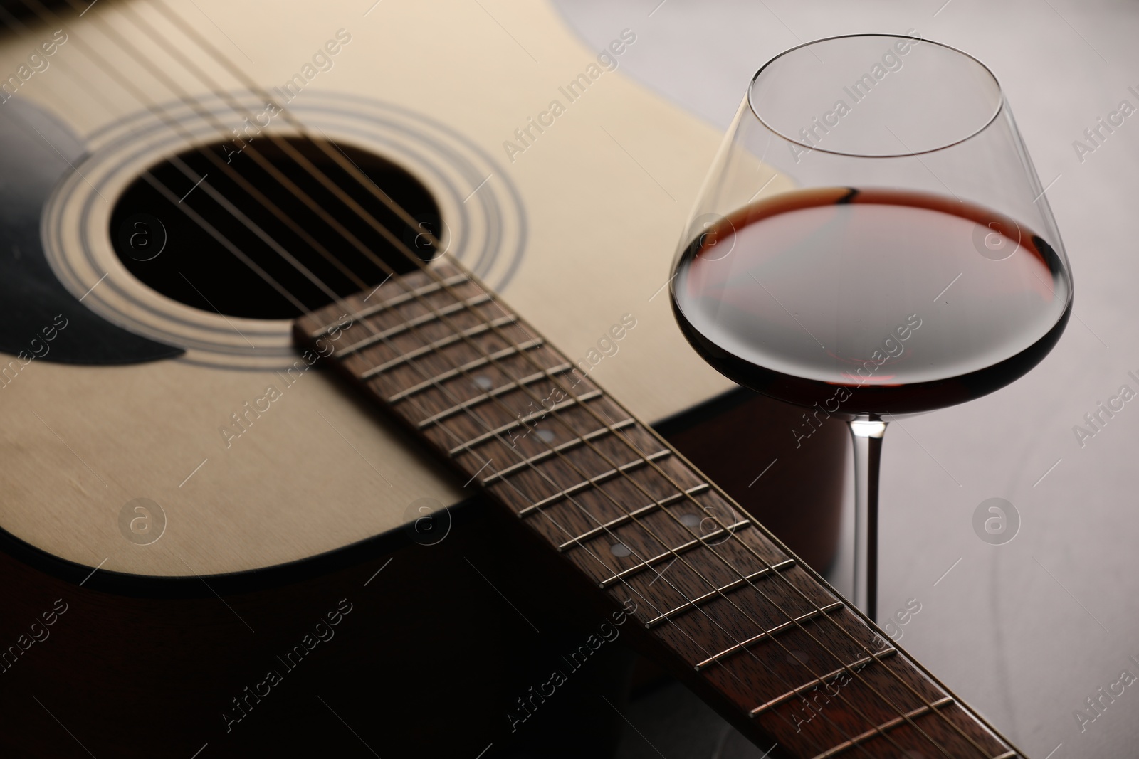 Photo of Acoustic guitar and red wine on grey table, closeup