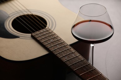 Photo of Acoustic guitar and red wine on grey table, closeup