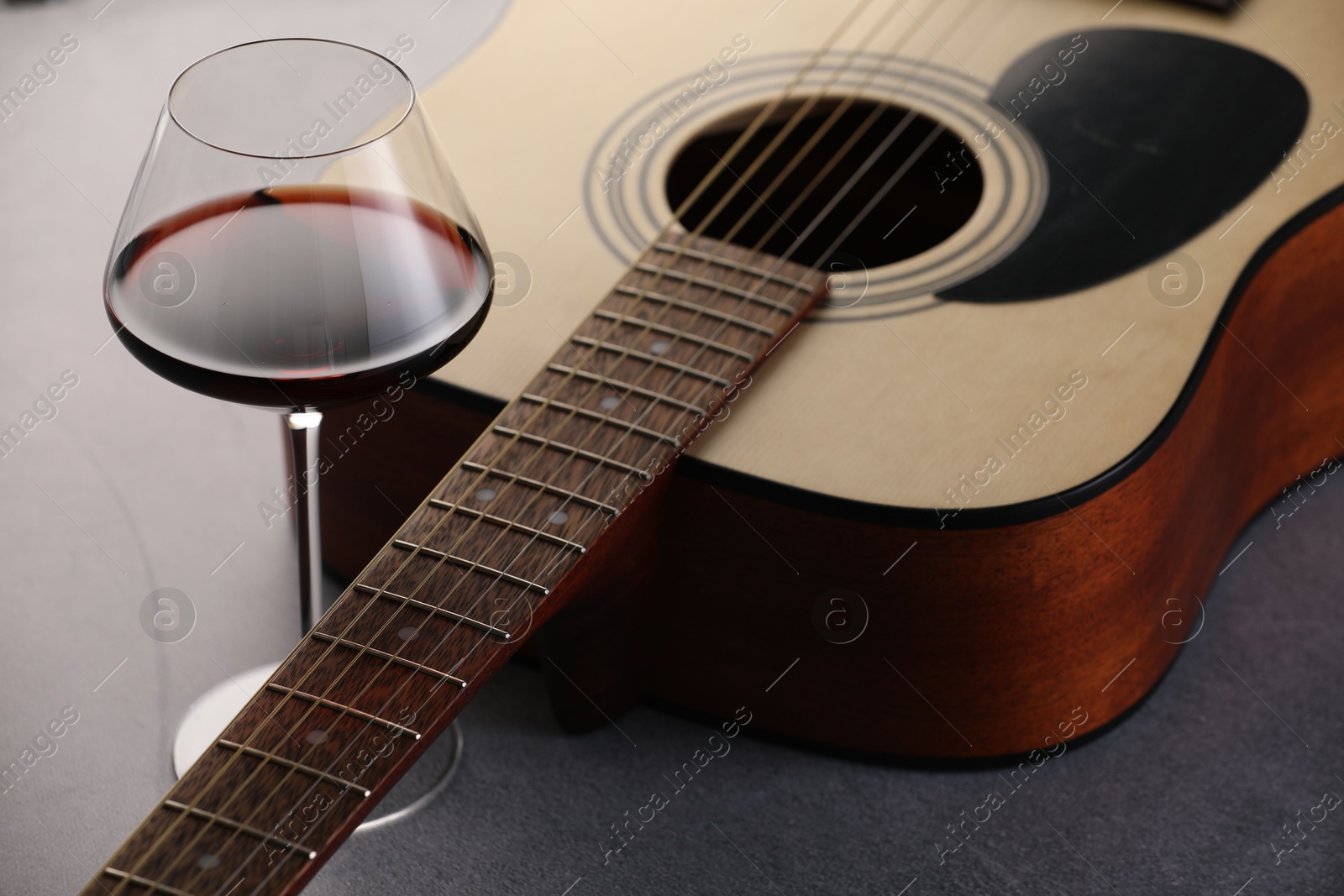 Photo of Acoustic guitar and red wine on grey table, closeup