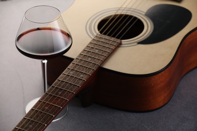 Photo of Acoustic guitar and red wine on grey table, closeup