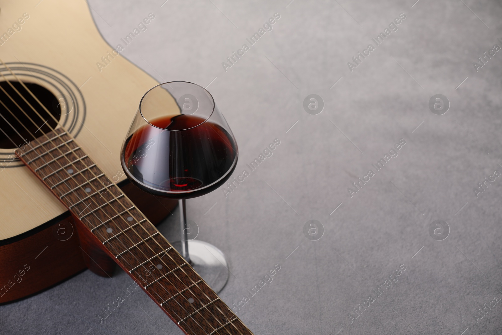 Acoustic guitar and red wine on grey table, closeup. Space for text Photo of Acoustic guitar and red wine on grey table, closeup. Space for text