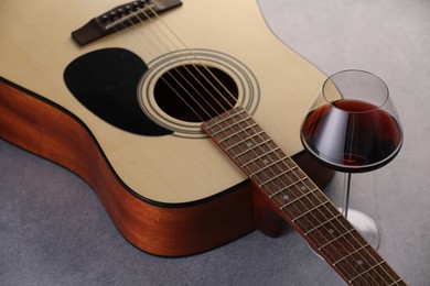 Photo of Acoustic guitar and red wine on grey table, closeup