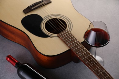 Photo of Acoustic guitar and red wine on grey table, closeup