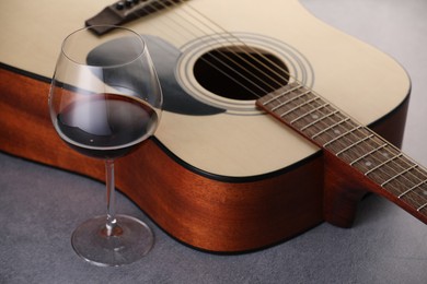 Photo of Acoustic guitar and red wine on grey table, closeup