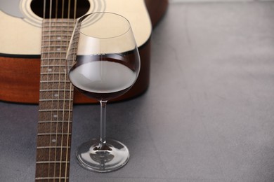 Photo of Acoustic guitar and red wine on grey table, closeup. Space for text