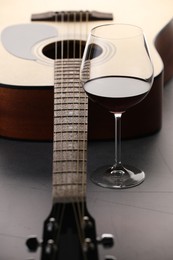 Photo of Acoustic guitar and red wine on grey table, closeup