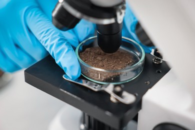 Photo of Scientist examining soil sample under microscope in laboratory, closeup