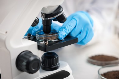 Photo of Scientist examining soil sample under microscope in laboratory, closeup