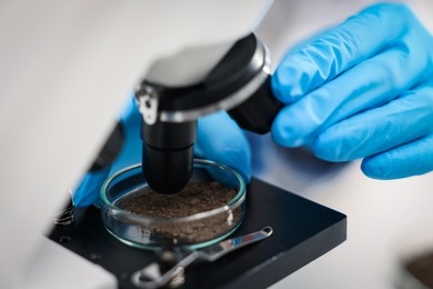 Photo of Scientist examining soil sample under microscope in laboratory, closeup