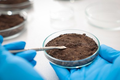 Photo of Scientist taking soil sample for research at table in laboratory, closeup