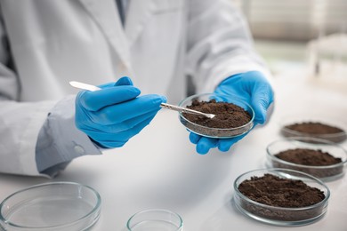 Photo of Scientist taking soil sample for research at white table in laboratory, closeup