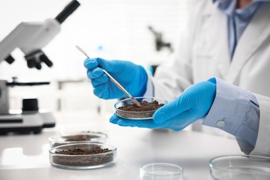 Photo of Scientist taking soil sample for research at white table in laboratory, closeup
