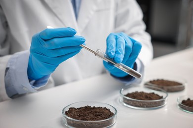 Photo of Scientist taking soil sample for research at white table in laboratory, closeup