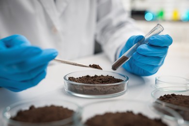 Photo of Scientist taking soil sample for research at white table in laboratory, closeup