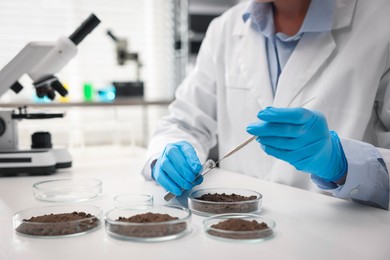 Photo of Scientist taking soil sample for research at white table in laboratory, closeup