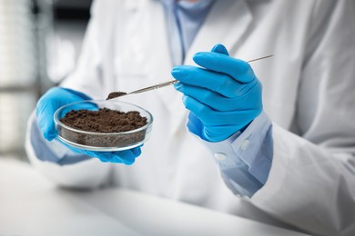 Photo of Scientist taking soil sample for research at white table in laboratory, closeup
