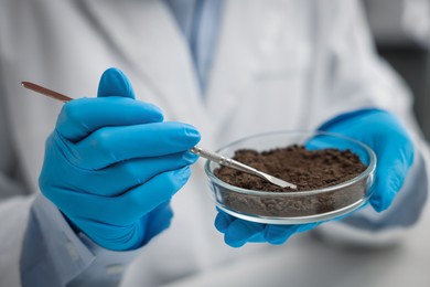 Photo of Scientist taking soil sample for research at table in laboratory, closeup