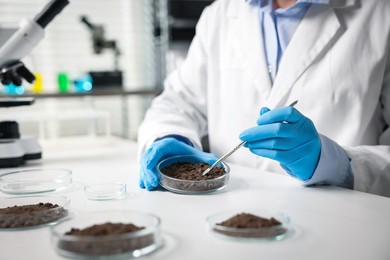 Photo of Scientist taking soil sample for research at white table in laboratory, closeup