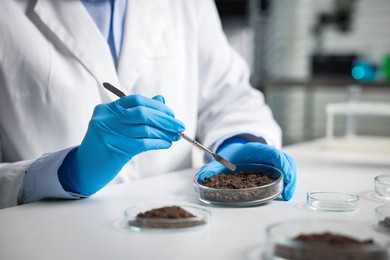 Photo of Scientist taking soil sample for research at white table in laboratory, closeup