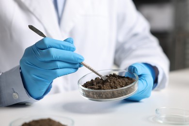 Photo of Scientist taking soil sample for research at white table in laboratory, closeup