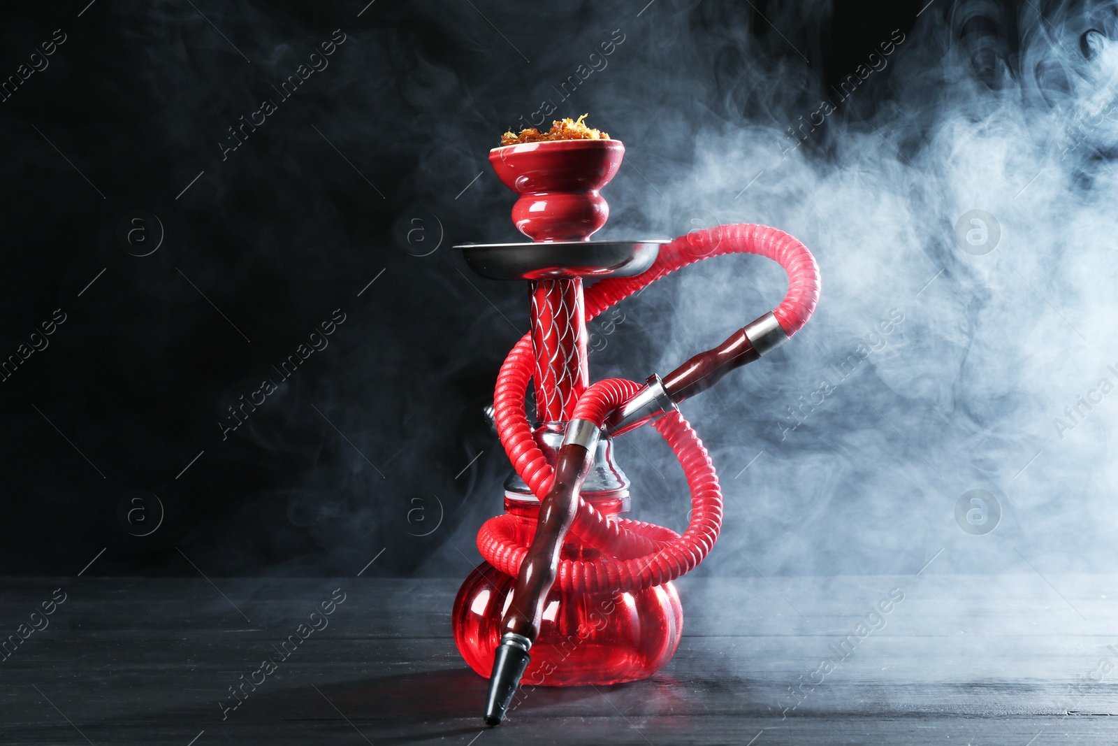 Hookah on wooden table with smoke against black background Photo of Hookah on wooden table with smoke against black background
