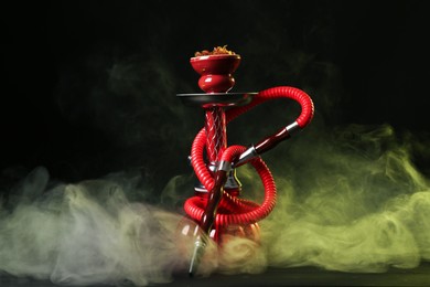 Photo of Hookah on wooden table with smoke against black background